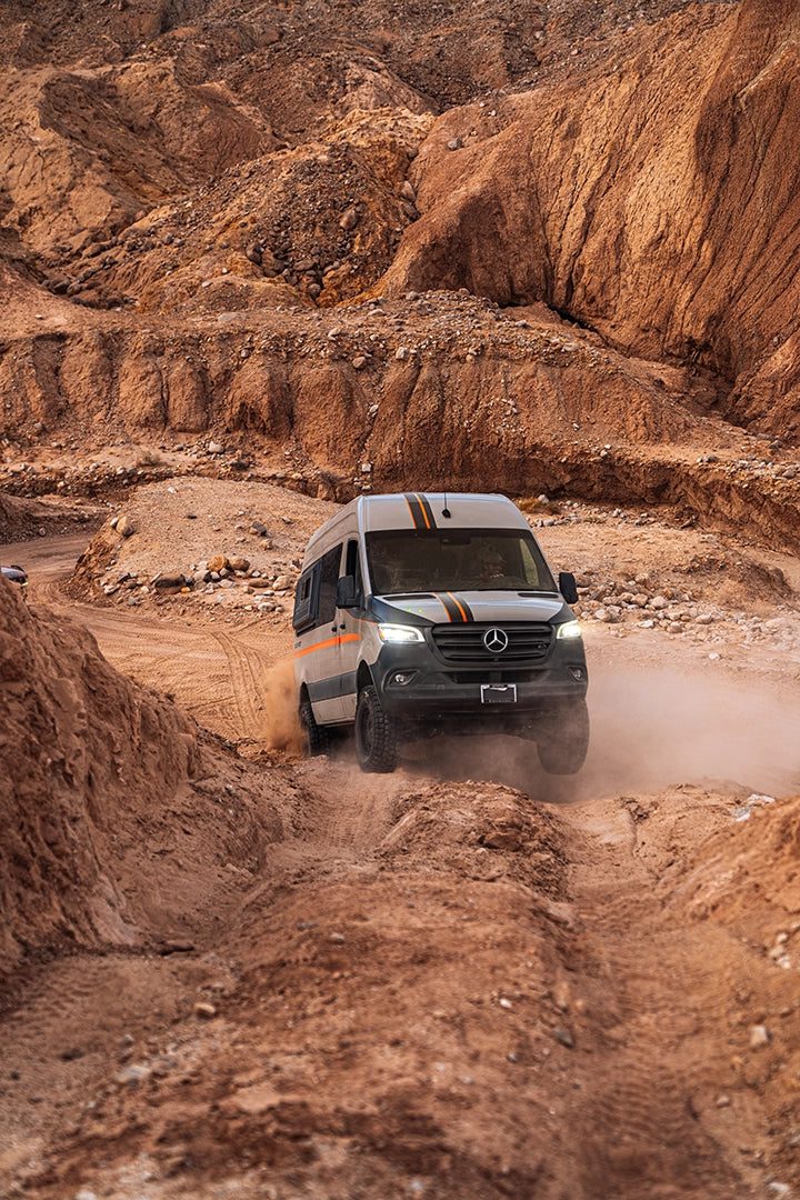 Van climbing a red dirt trail in desert terrain