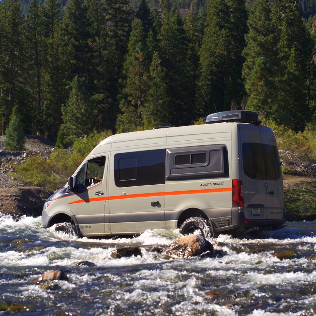 Van crossing a rocky river in a pine forest