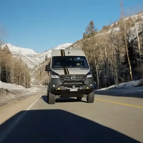 Van driving a mountain road between snowy peaks
